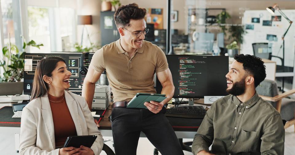Agenturteam bespricht sich lachend im Büro vor Monitoren mit Programmcode