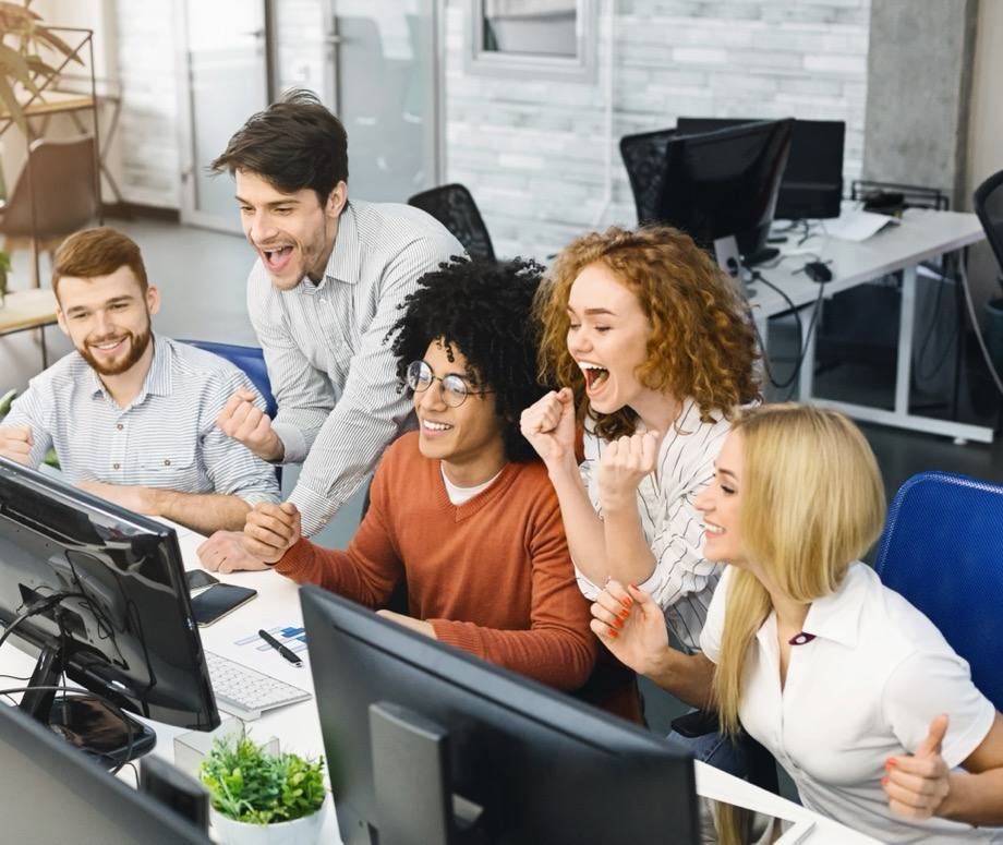 Begeistertes Team jubelt im Büro gemeinsam vor dem Bildschirm über einen Erfolg